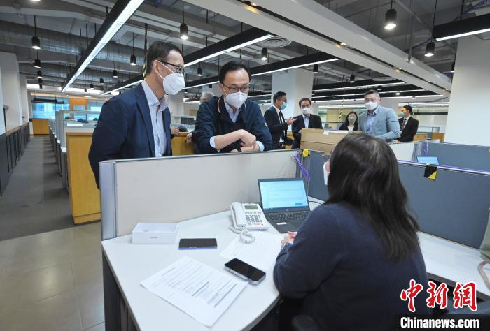 聶德權(quán)(左二)與在電話熱線中心協(xié)助市民登記“疫苗到戶接種服務(wù)”的明愛專上學(xué)院學(xué)生交談?！∠愀厶貐^(qū)政府新聞處供圖