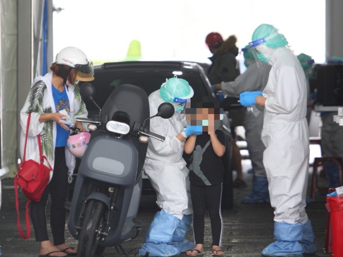 本土疫情升溫，一位家長帶著小孩騎車前往排隊篩檢。（張鎧乙攝）