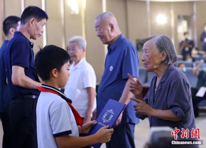圖片南京大屠殺幸存者夏淑琴(右一)、葛道榮(右二)、艾義英(右三)向南京大屠殺幸存者后代代表頒發(fā)“南京大屠殺歷史記憶傳承人”證書。泱波 攝