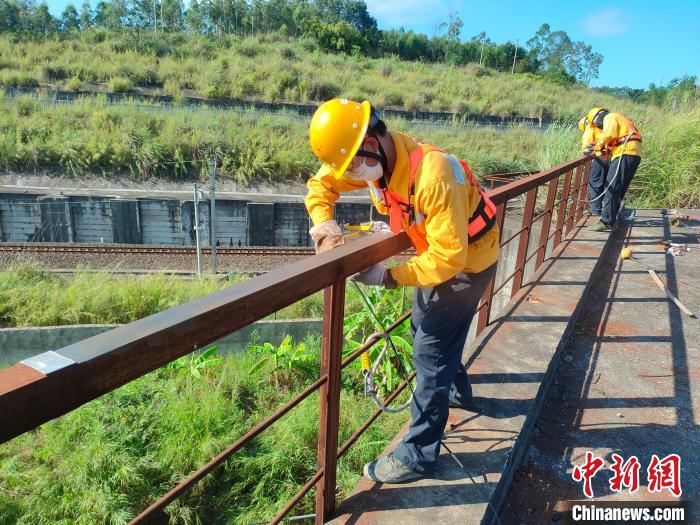 圖為高溫下南寧工務(wù)段橋梁工全副武裝對鐵路橋梁人行道欄桿打磨除銹?！●T博 攝